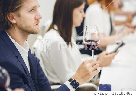 Professional looking sommelier tasting red wine from glass, analysing its taste, color, smell and acidity level. Wine expert studies wine geographic and area on winemaking lecture.  133192466
