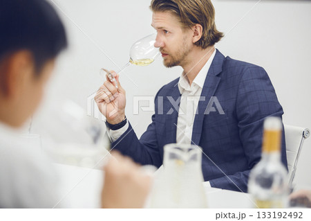 Attractive and mature looking male sommelier tests white wine in a glass during a tasting or winemaking training. 133192492