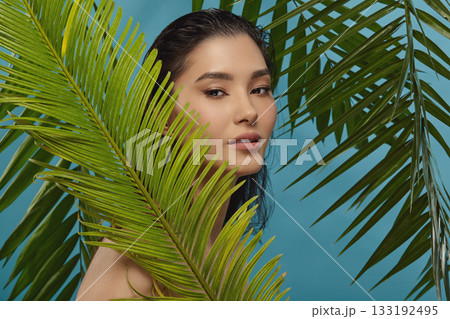 Well groomed woman peeks out from behind palm leaves. Well groomed woman peeks out from behind palm leaves. 133192495