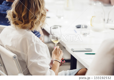 Back portrait of female sommelier holding white wine in glass and tasting it during wine expert training. Alcoholic beverages masterclass, professional development for restaurant staff.  133192532
