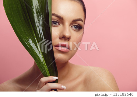 beautiful woman holds tropical leaf near her face on a pink isolated 133192540
