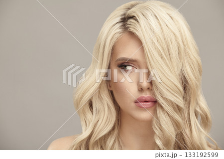 Blonde woman with long wavy hair looks aside on beige isolated background with free copy space. 133192599
