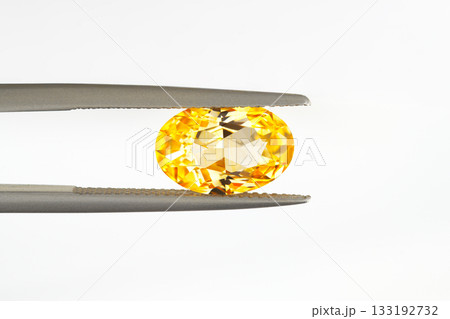A yellow gemstone is being held up by a metal clamp 133192732
