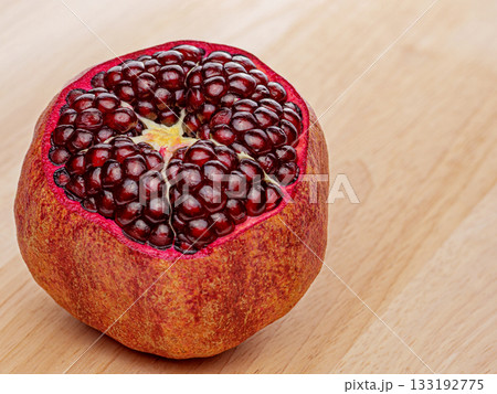 A red pomegranate is cut in half and placed on a wooden table A red pomegranate is cut in half and placed on a wooden table 133192775