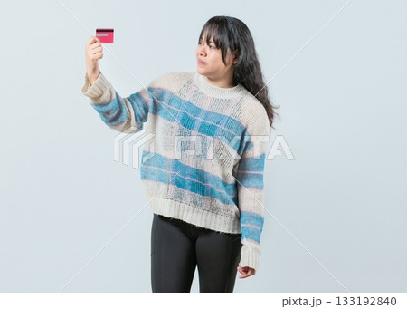 Confused asian girl holding a credit card isolated. Unsure and confused young woman holding and looking at a credit card 133192840