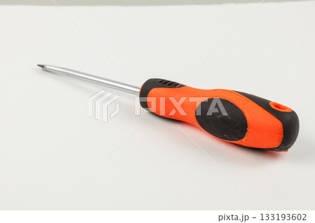 Screwdriver with an orange and black handle on a white surface Screwdriver with an orange and black handle on a white surface 133193602