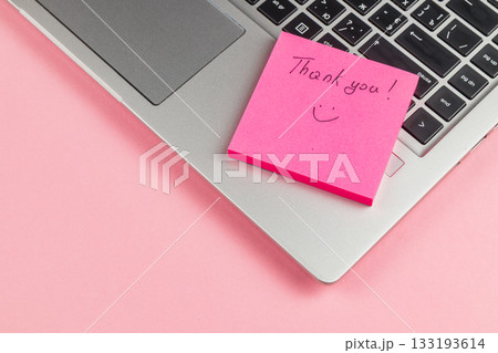 Thank you note on pink sticky pad next to laptop on a pink background 133193614