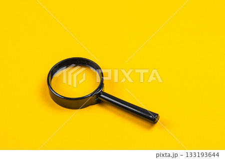 Simple black magnifying glass against a bright yellow background 133193644