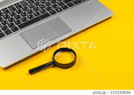 Laptop and magnifying glass on bright yellow surface for clear visuals 133193646