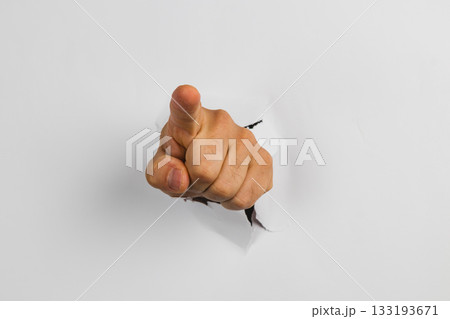 Hand pointing through a hole in white wall creating a striking visual effect 133193671