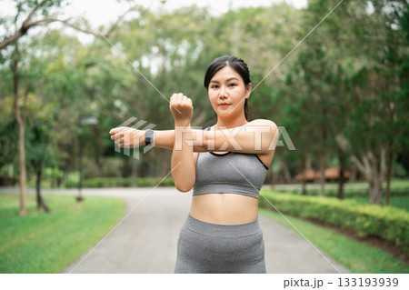 Fit woman stretching her arms outdoors in a park wearing athletic wear, promoting health and fitness lifestyle in a serene environment 133193939