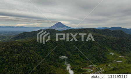 Top view of farmland and active Sinabung volcano. Agricultural landscape in Sumatra. Berastagi, Indonesia. Top view of farmland and active Sinabung volcano. Agricultural landscape in Sumatra. Berastagi, Indonesia. 133195315