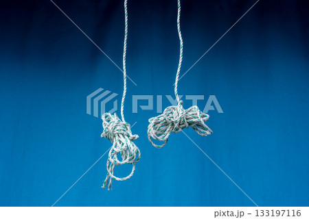 Two knotted ropes hanging against blue background Two knotted ropes hanging against blue background 133197116