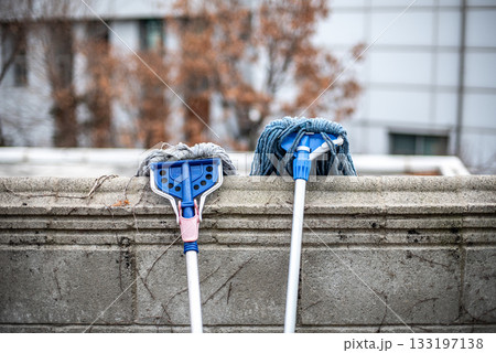Two mops leaning against a concrete wall outdoors in Seoul, South Korea Two mops leaning against a concrete wall outdoors in Seoul, South Korea 133197138