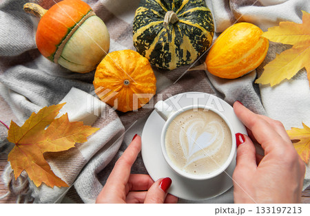 Hands holding coffee with heart latte art among autumn pumpkins Hands holding coffee with heart latte art among autumn pumpkins 133197213