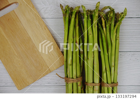 Bunch of fresh green asparagus stems with cutting wooden board on wooden background 133197294