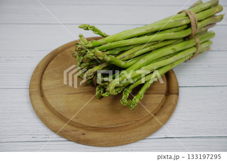 Bunch of fresh green asparagus stems with cutting wooden board on wooden background Bunch of fresh green asparagus stems with cutting wooden board on wooden background 133197295