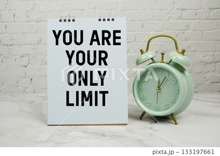 "You Are Your Only Limit" with green vintage alarm clock against a white brick wall background. 133197661