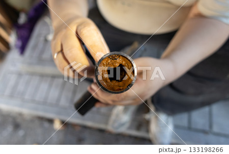 A person's hands hold a section of an old, rusted water pipe, revealing heavy rust and mineral deposits. The buildup of limescale and rust obstructs the flow of water through the pipe. 133198266