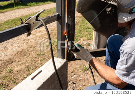 Male adult welding metal frame outdoors with protective gear. National Welding Month Male adult welding metal frame outdoors with protective gear. National Welding Month 133198525