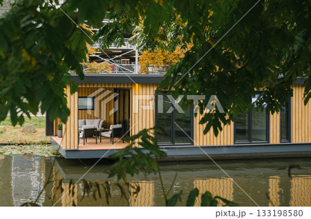 Modern floating home on a tranquil lake surrounded by lush greenery Modern floating home on a tranquil lake surrounded by lush greenery 133198580
