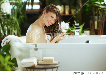Happy Woman Applying Hair Product in Bathtub 133200334