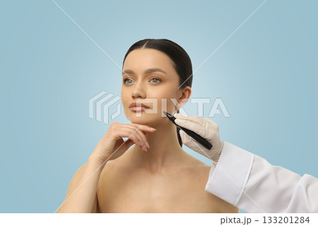 A beautician prepares a client for a facial procedure with markings 133201284