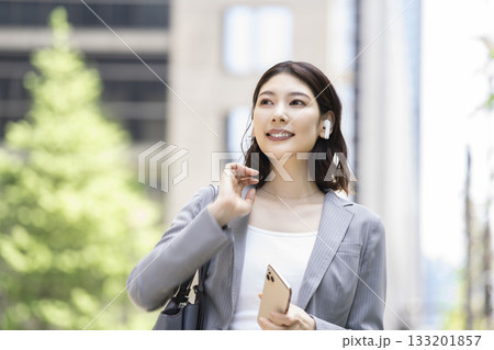 イヤホンをつけスマートフォンを持ったビジネスウーマン イヤホンをつけスマートフォンを持ったビジネスウーマン 133201857