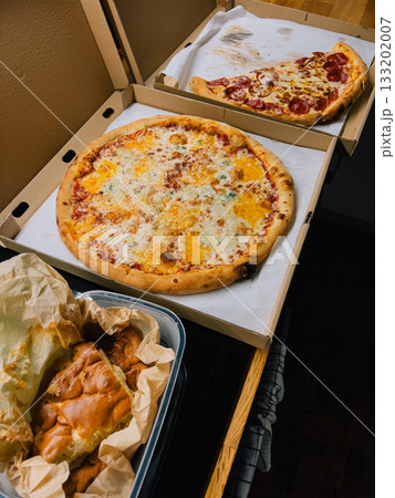 Two whole pizzas featuring variety of toppings alongside some focaccia bread sit in plastic container on kitchen counter, awaiting enjoyment for lunch or dinner. Two big pizzas and focaccia bread 133202007