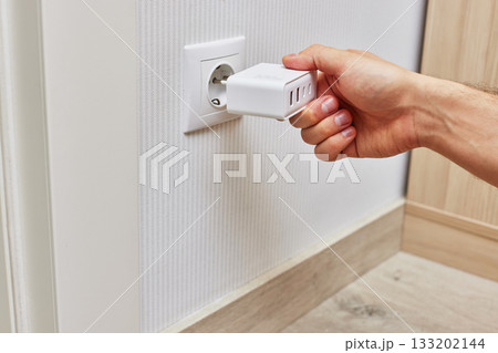 male hand insert a plug of the phone charger into socket at home male hand insert a plug of the phone charger into socket at home 133202144