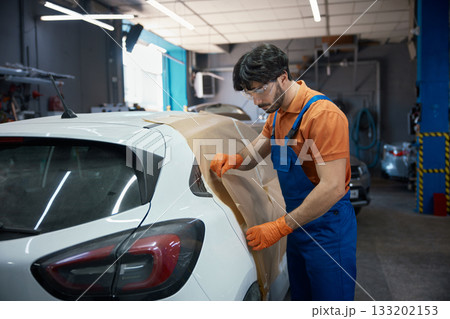 Automotive technician prepping compact car in garage for paint and bodywork refinishing 133202153