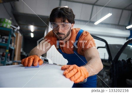 Auto body technician sanding car panel in workshop Auto body technician sanding car panel in workshop 133202156