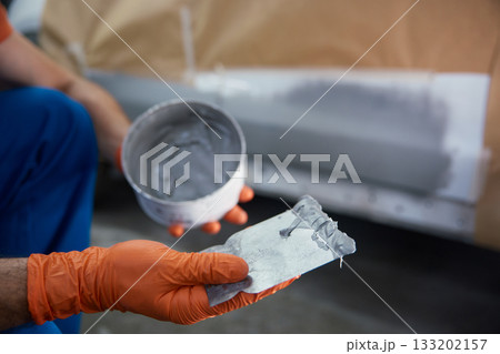 Closeup of technician is meticulously prepping a car panel with primer in a garage workshop Closeup of technician is meticulously prepping a car panel with primer in a garage workshop 133202157