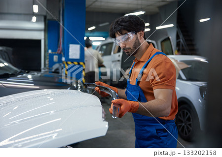 Auto body technician repairing car hood in professional garage workshop with safety gear Auto body technician repairing car hood in professional garage workshop with safety gear 133202158