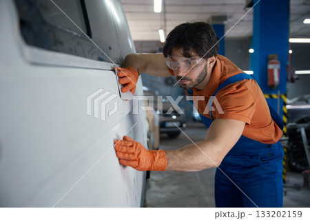 An auto body technician is meticulously inspecting a car panel in the repair shop today An auto body technician is meticulously inspecting a car panel in the repair shop today 133202159