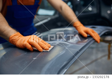 Auto technician sanding car body panel with orange gloves in workshop 133202178