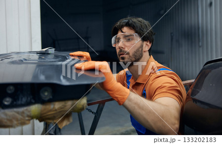 Technician worker skillfully restoring a car door in a busy garage workshop space 133202183