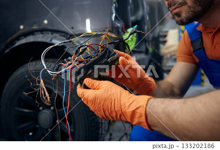 Mechanic inspecting complex car wiring harness in garage Mechanic inspecting complex car wiring harness in garage 133202186