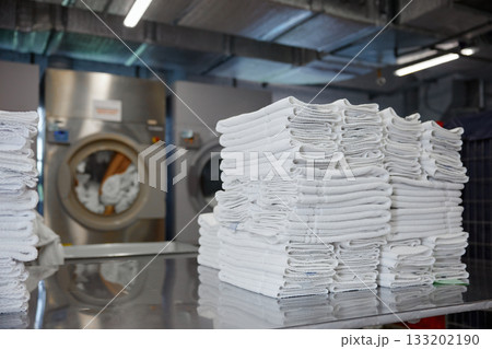 A stack of clean towels is on a table in front of a washing machine 133202190