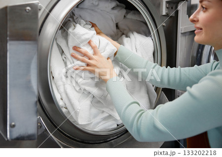 A woman worker is loading various clothes into a washing machine A woman worker is loading various clothes into a washing machine 133202218