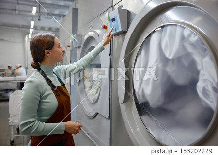 A woman is pressing down on a button on a washing machine 133202229
