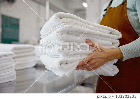 Closeup of a woman worker in an apron holds fresh towels in a laundromat Closeup of a woman worker in an apron holds fresh towels in a laundromat 133202233