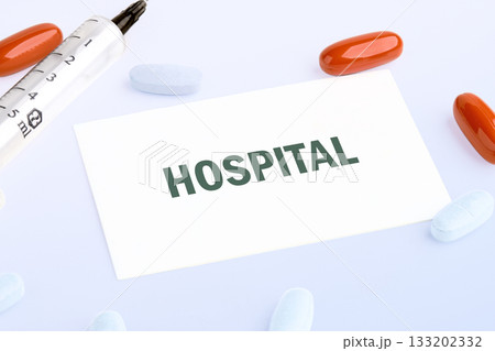Medical treatment idea with a syringe, red and white pills, and a note with the word Hospital on a white background, suggesting care and medication Medical treatment idea with a syringe, red and white pills, and a note with the word Hospital on a white background, suggesting care and medication 133202332