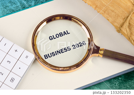 A magnifying glass focuses on Global Business 2026 lying on top of a notepad with a calculator and wrapped material near by. The background has a teal color to it A magnifying glass focuses on Global Business 2026 lying on top of a notepad with a calculator and wrapped material near by. The background has a teal color to it 133202350
