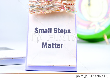 A desk calendar sits open, displaying the motivational message Small Steps Matter, while nearby, a calculator and a clock suggest a focus on time and progress A desk calendar sits open, displaying the motivational message Small Steps Matter, while nearby, a calculator and a clock suggest a focus on time and progress 133202419