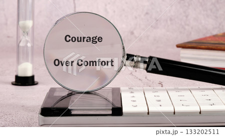 A magnifying glass highlights the phrase Courage Over Comfort on a calculator. An hourglass and books set the scene, emphasizing time and knowledge in the pursuit of bravery A magnifying glass highlights the phrase Courage Over Comfort on a calculator. An hourglass and books set the scene, emphasizing time and knowledge in the pursuit of bravery 133202511