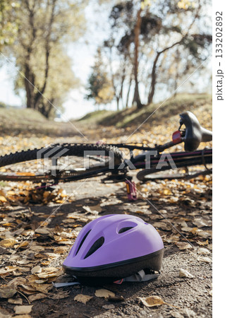 Purple helmet lies abandoned on the pavement beside a toppled bicycle, evidence of a sudden fall. Purple helmet lies abandoned on the pavement beside a toppled bicycle, evidence of a sudden fall. 133202892