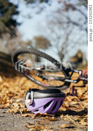 Purple helmet lies abandoned on the pavement beside a toppled bicycle, evidence of a sudden fall. Purple helmet lies abandoned on the pavement beside a toppled bicycle, evidence of a sudden fall. 133202901