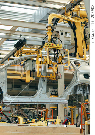 White car body is suspended on a yellow automated lift within a vast, multi-level automotive assembly plant White car body is suspended on a yellow automated lift within a vast, multi-level automotive assembly plant 133202908