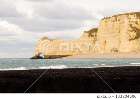 Limestone sea cliffs and natural arch at Etretat, Normandy, framed by ocean waves and a calm coastal landscape. 133204606